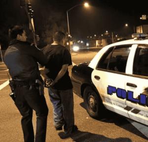 A police officer arresting a man next to a patrol car at night, hihglighting DUI and Minor in Possession (MIP) laws in Georgia
